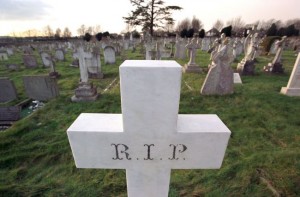 A white cross in a graveyard showing the letters R I P